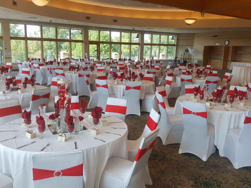 white covered chairs with red sash and red floral centerpiece